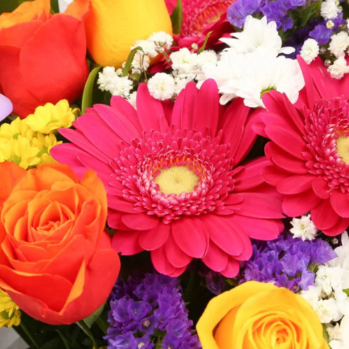 “Bright bouquet with yellow roses, pink gerberas, purple freesias, and white daisies wrapped in white paper – under £35 UK flower delivery.”