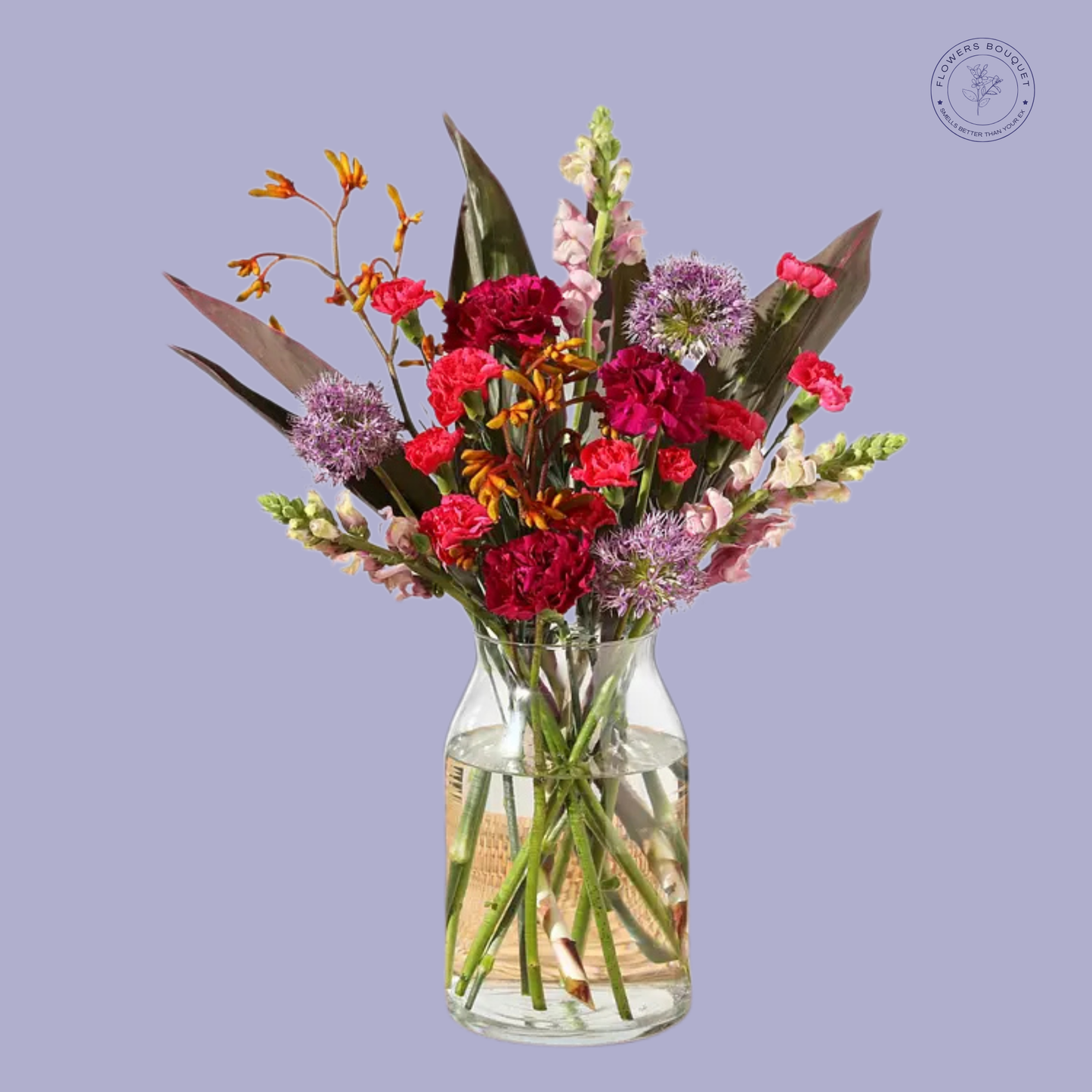 An exotic bouquet called "Exotic Sunset," featuring red carnations, orange crocosmia, pink snapdragons, purple alliums, and tropical foliage in a clear glass vase.