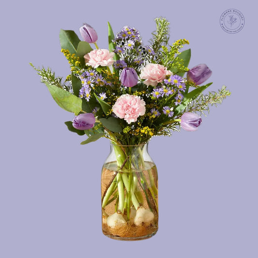 A beautiful floral arrangement featuring 19 stems, including pink carnations, purple tulips, rosemary, and solidago, arranged in a glass vase with visible roots for a natural touch.