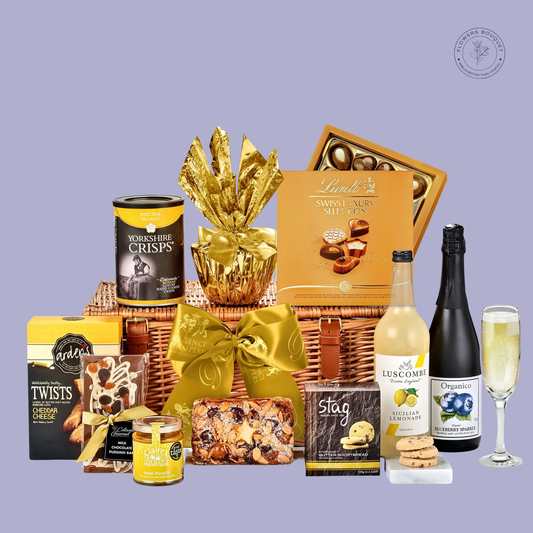  A luxurious golden gift basket featuring alcohol-free sparkling drinks, Yorkshire crisps, Swiss chocolates, cheddar twists, and festive treats, elegantly wrapped in a golden ribbon.