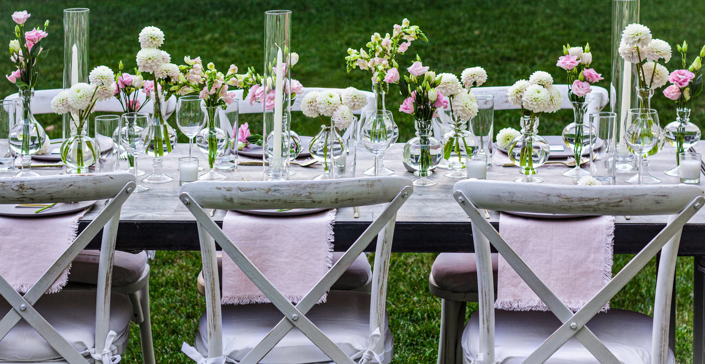 Elegant garden dining table with pink and white floral arrangements, candles, and modern tableware, ideal for outdoor events.