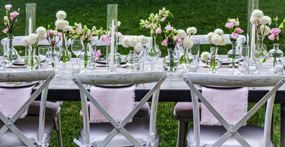 Elegant garden dining table with pink and white floral arrangements, candles, and modern tableware, ideal for outdoor events.