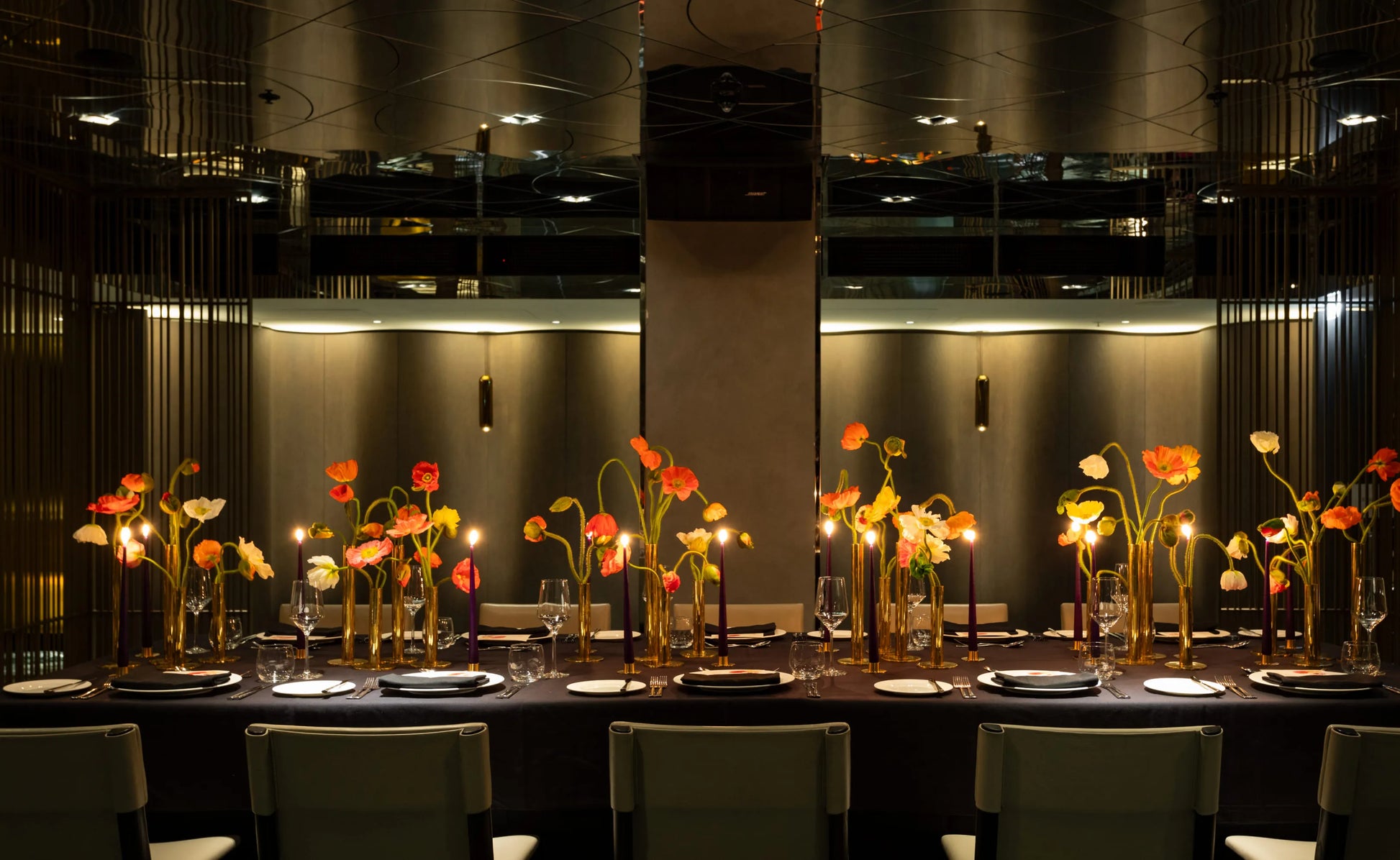 Elegant floral centerpiece with colorful poppies in gold candle holders on a formal dining table.
