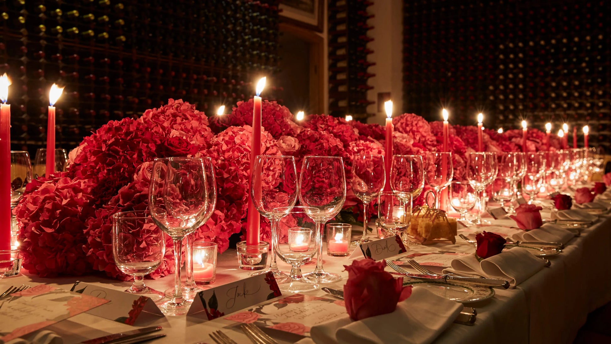 Elegant floral table centerpiece with red hydrangeas, red roses, and candles for luxury event decor.