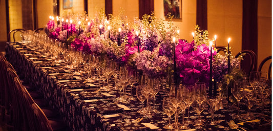 Elegant floral table setting with purple orchids, white flowers, and tall black candles for a luxury event.