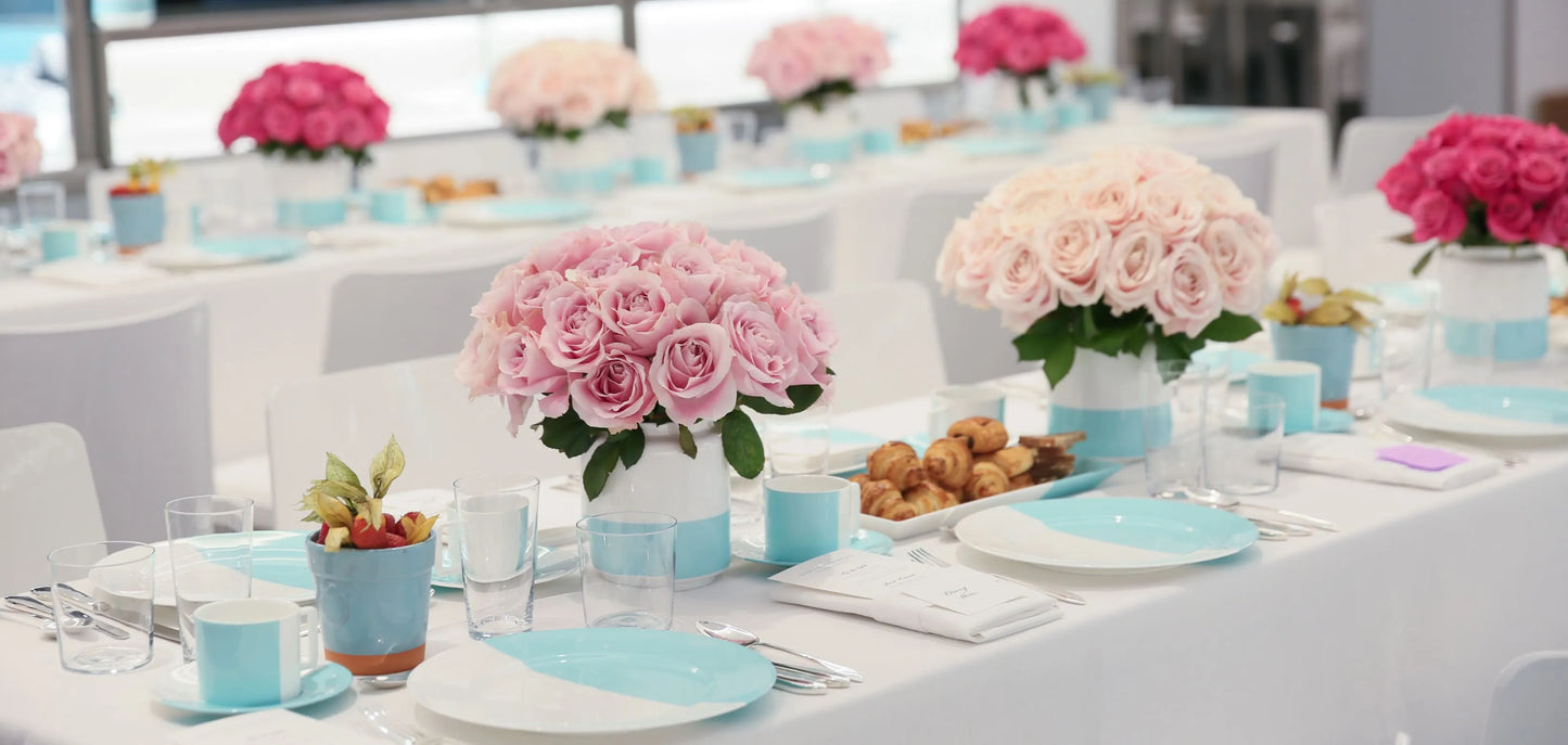 Elegant dining table setup with pink roses, turquoise tableware, and glassware, perfect for weddings and elegant events.
