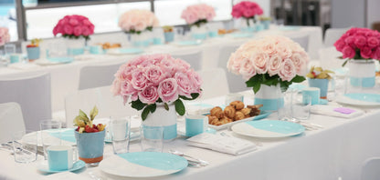 Elegant dining table setup with pink roses, turquoise tableware, and glassware, perfect for weddings and elegant events.

