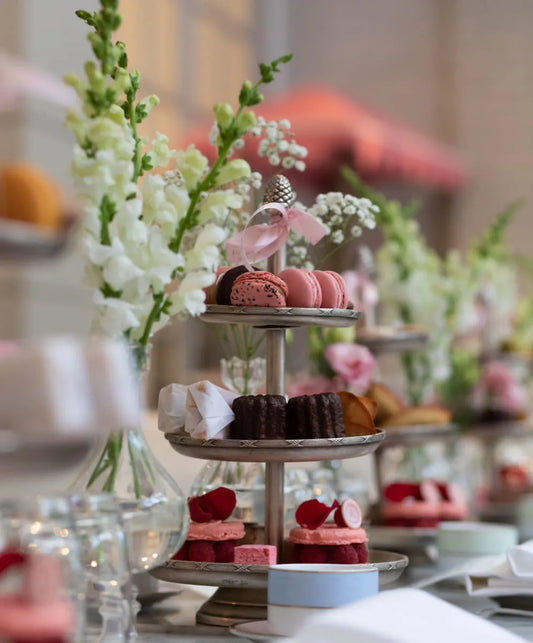 Elegant tea party table setup with pink roses, macarons, tiered dessert stands, and blue and white tea cups, perfect for celebrations.
