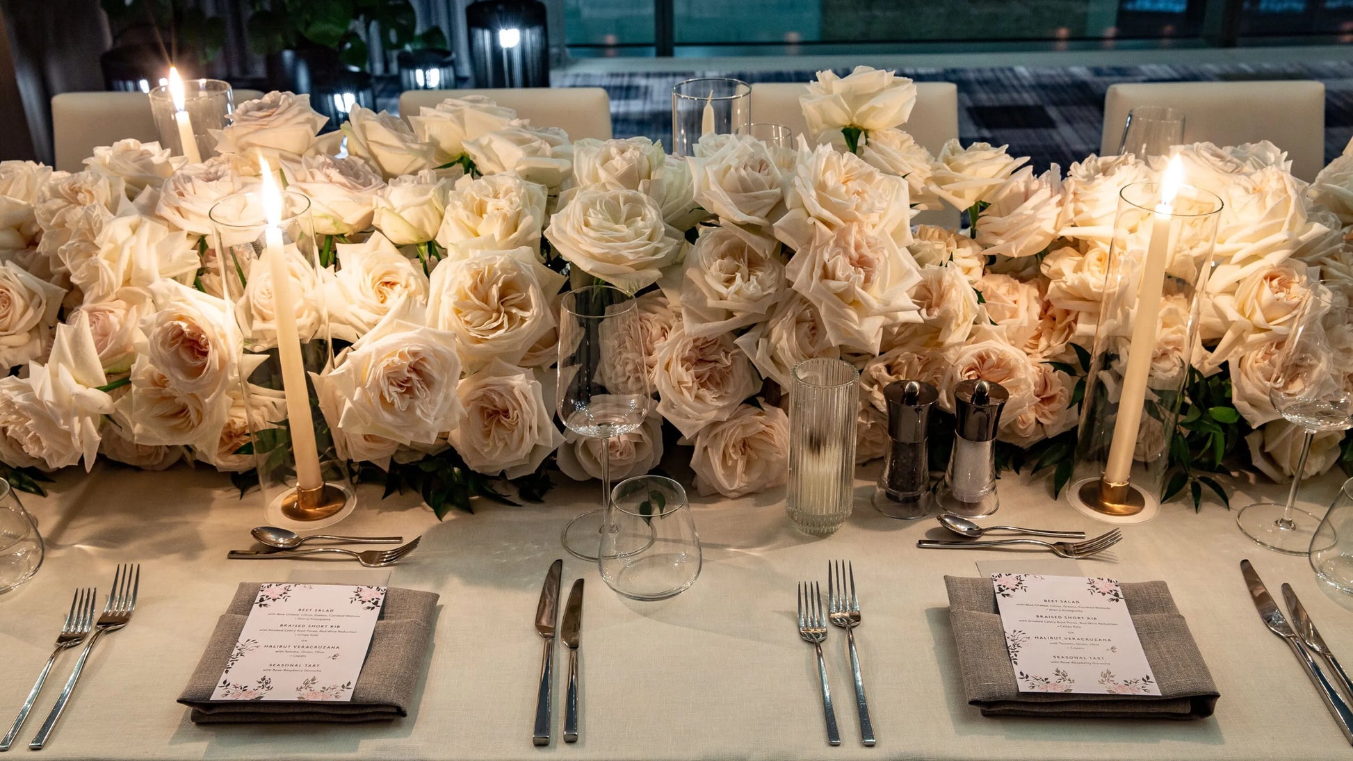 Elegant white rose table arrangement with candles and fine tableware, perfect for upscale events.