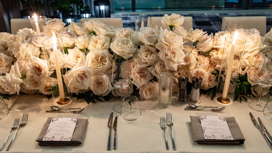 Elegant white rose table arrangement with candles and fine tableware, perfect for upscale events.