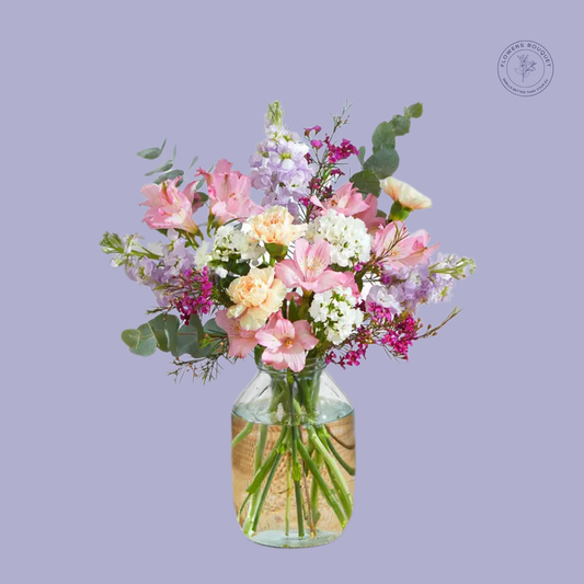 A delicate floral arrangement called "Eternal Grace," showcasing pastel alstroemeria, peach carnations, white hydrangeas, and eucalyptus in a clear glass vase with water.