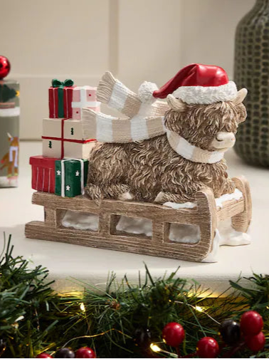Highland cow Christmas decoration with Santa hat, scarf, and sleigh carrying festive gifts