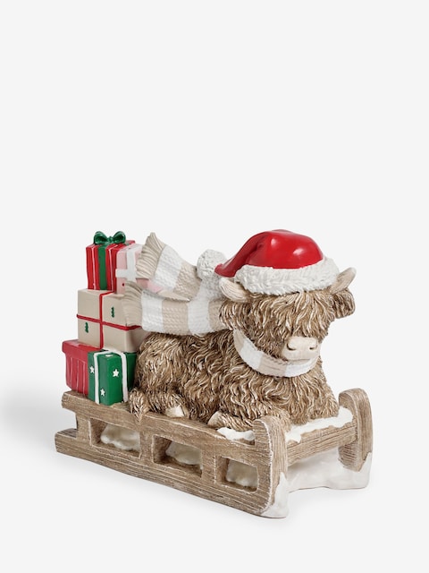 Highland cow Christmas decoration with Santa hat, scarf, and sleigh carrying festive gifts