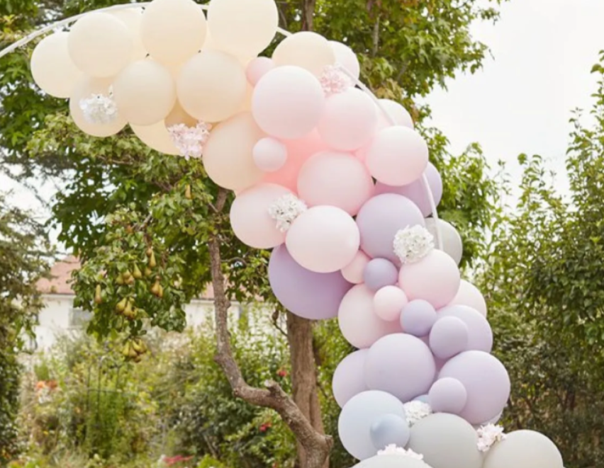 Pastel balloon arch for garden party decoration with pink, lavender, and cream balloons outdoors.