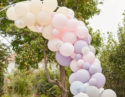 Pastel balloon arch for garden party decoration with pink, lavender, and cream balloons outdoors.