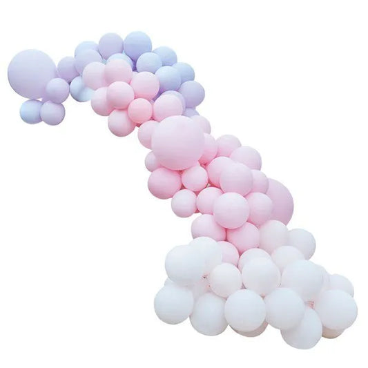 Pastel balloon arch in soft rainbow colours, outdoor party decoration setup with pink, lilac, peach, and cream balloons.