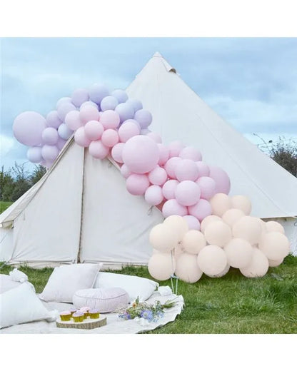 Pastel balloon arch in soft rainbow colours, outdoor party decoration setup with pink, lilac, peach, and cream balloons.