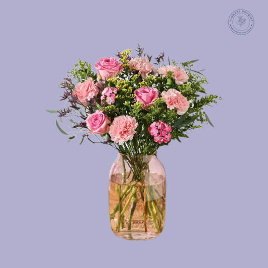 A delightful bouquet called "Pink Delight," featuring pink roses, carnations, spray carnations, solidago, and seasonal greenery in a pink-tinted glass vase.