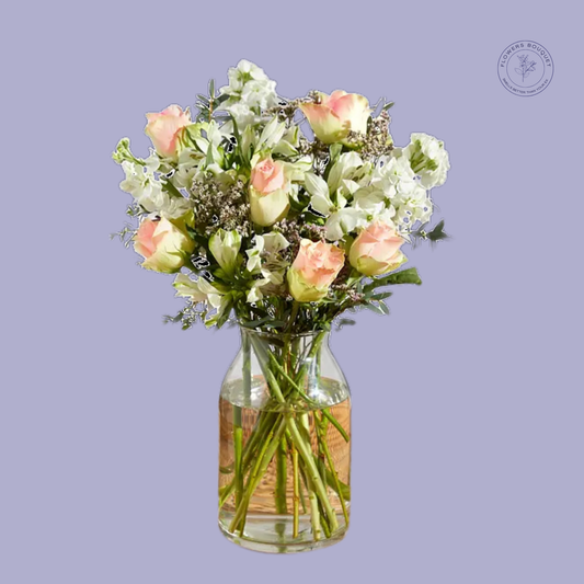 A serene floral arrangement called "Pure Serenity," featuring peach roses, white alstroemeria, and lush greenery in a clear glass vase with water.