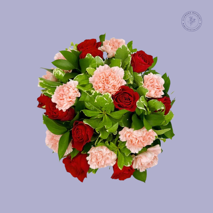 Red roses and pink carnations bouquet with lush greenery in a clear vase.
