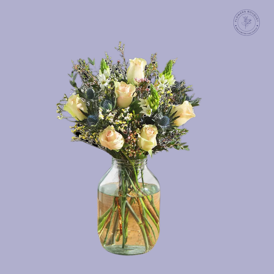 A sophisticated floral arrangement called "Seasonal Elegance Bouquet," featuring 19 stems of cream roses, waxflowers, ornithogalum, and limonium, displayed in a clear glass vase with visible water and stems.