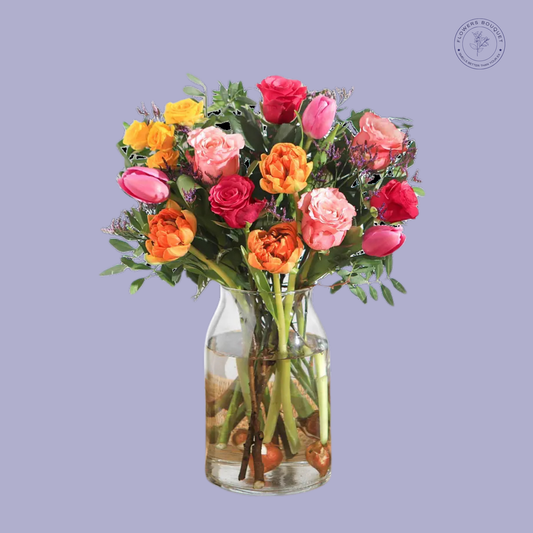 A vibrant floral arrangement called "Summer Blossom Delight," showcasing colorful roses, orange ranunculus, and pink tulips in a clear vase with visible stems and water.