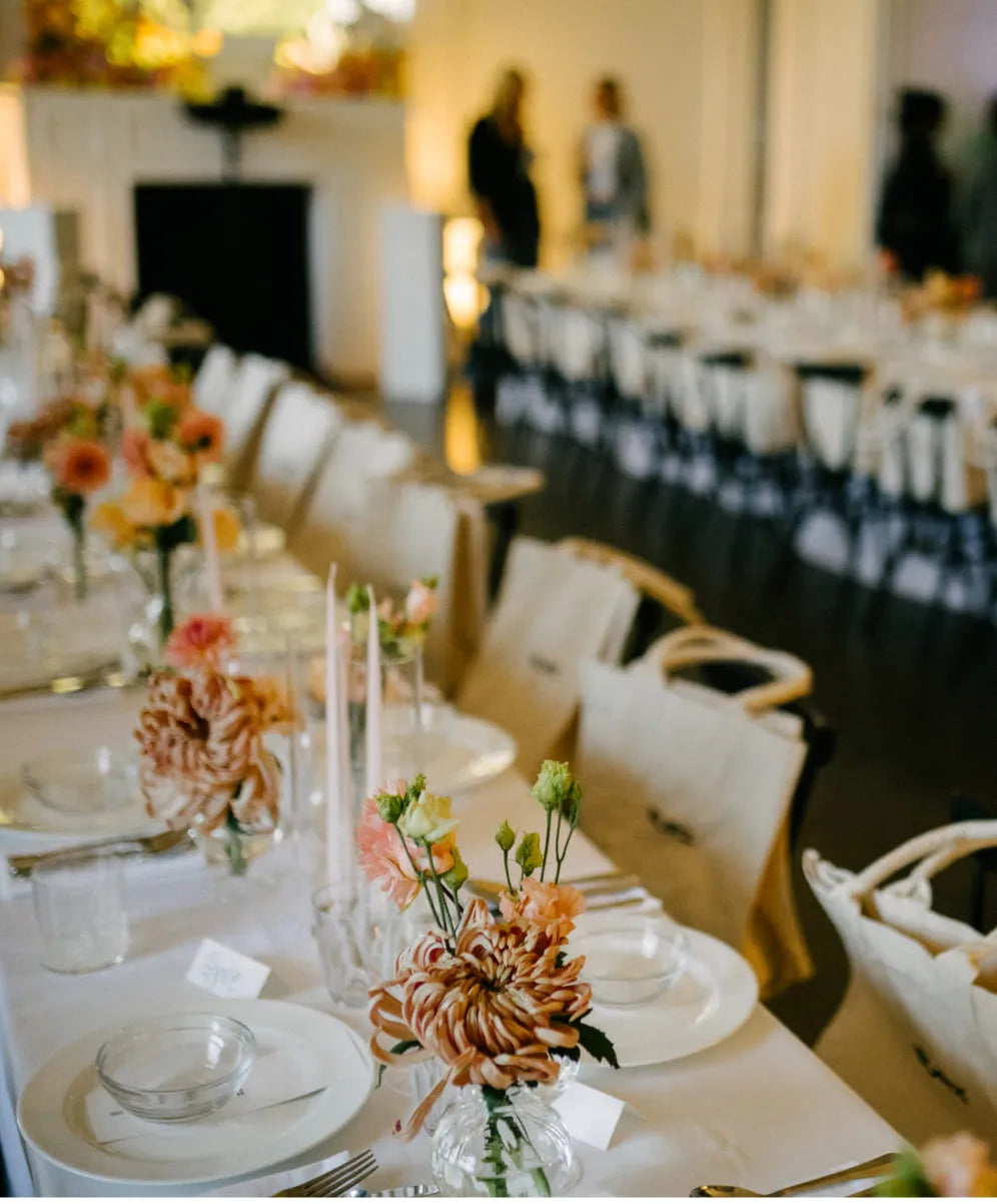Peachy-pink flowers with greenery in glass vases, ideal for elegant event table decor.