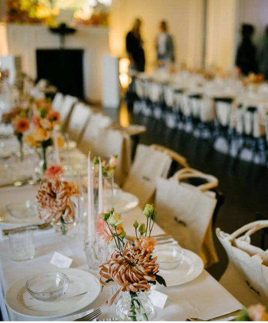 Peachy-pink flowers with greenery in glass vases, ideal for elegant event table decor.